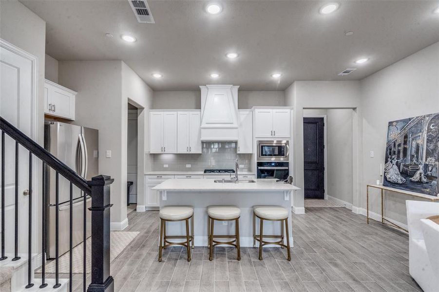 Kitchen with premium range hood, tasteful backsplash, a center island with sink, and appliances with stainless steel finishes