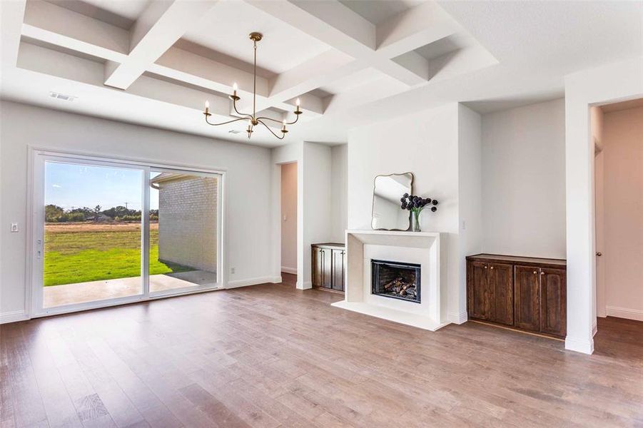 Unfurnished living room with coffered ceiling, beam ceiling, light wood finished floors, a fireplace, and a chandelier Unfurnished living room with coffered ceiling, beam ceiling, light wood finished floors, a fireplace, and a chandelier
