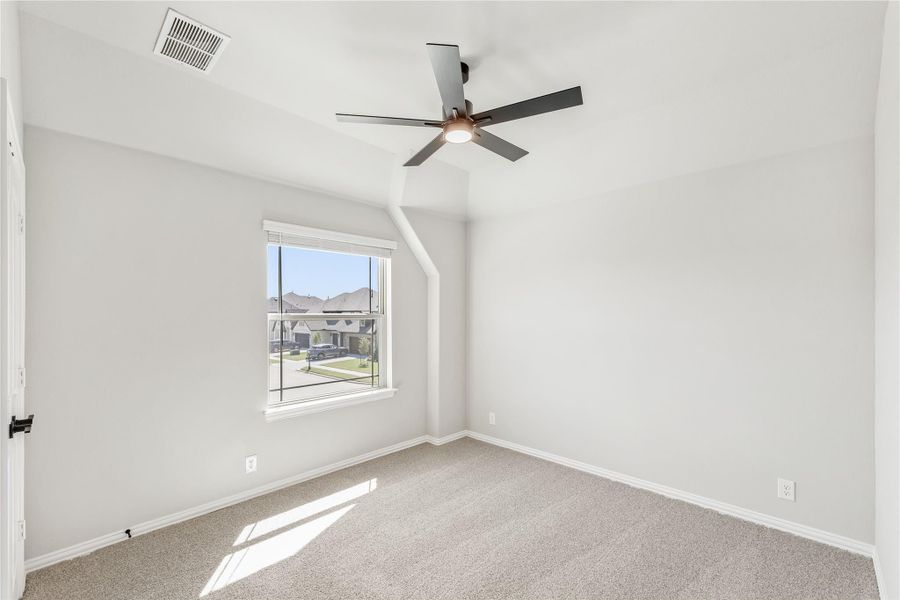 Empty bedroom with vaulted ceiling, ceiling fan, carpet flooring, and a window overlooking the neighborhood