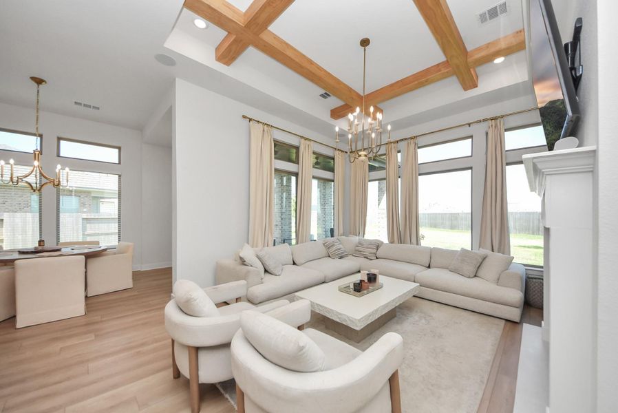 Bright and spacious living area featuring a cozy sectional, elegant chandelier, and large windows that offer abundant natural light, seamlessly connected to a stylish dining space.