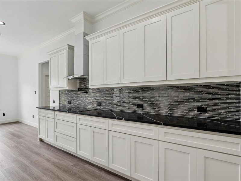 Kitchen featuring tasteful backsplash, light hardwood / wood-style floors, white cabinetry, dark stone counters, and wall chimney range hood