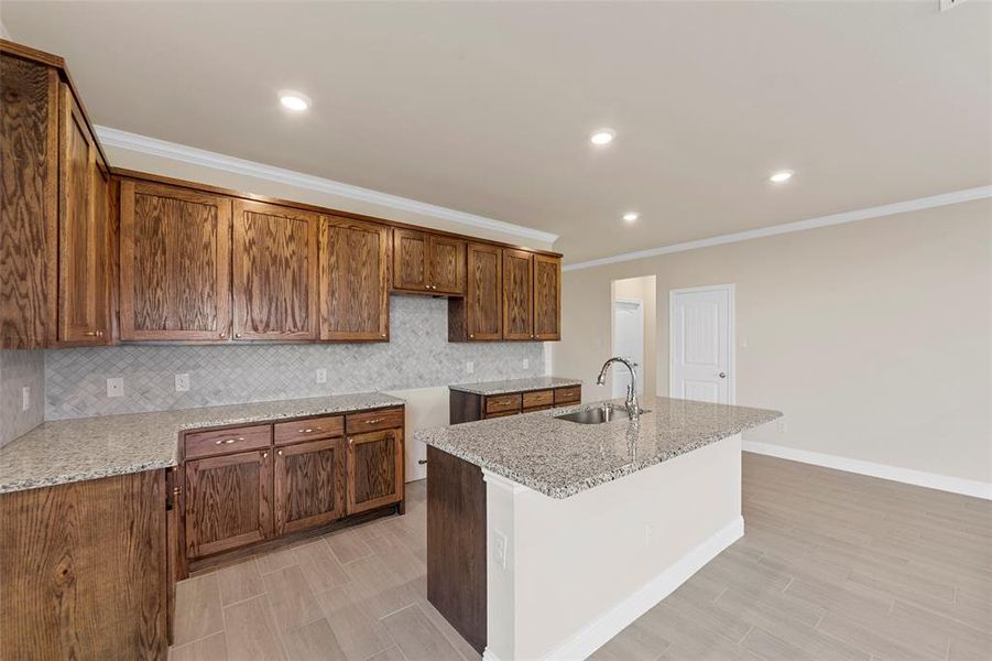 Kitchen featuring light stone countertops, an island with sink, crown molding, and sink