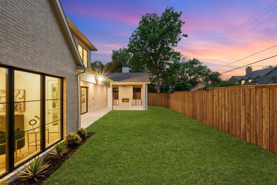 This property features an expansive lawn, a stone patio with a fireplace, and a privacy fence