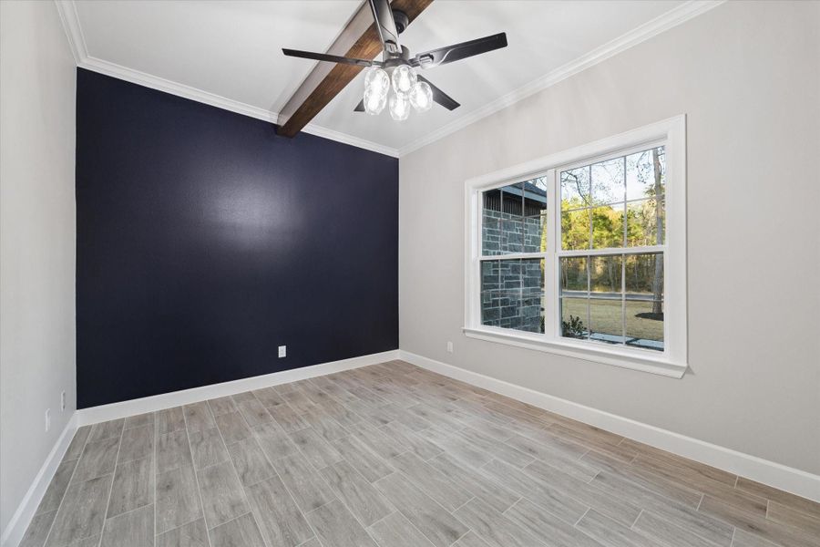 Home office with high beam ceiling and lighted ceiling fan. Designer blue accent wall.  Large window looks to the front of the home.   Wood look ceramic tile flooring.