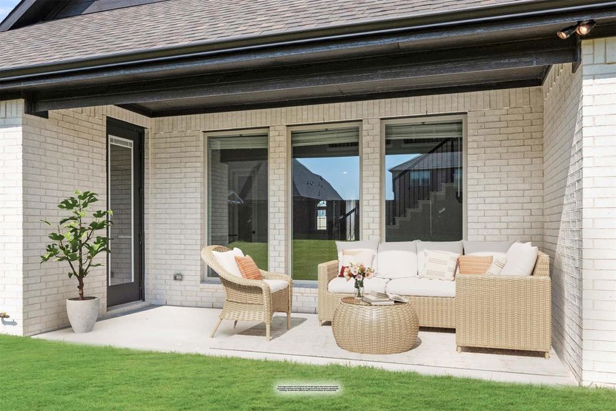 Covered back patio with wicker seating set on white brick home with large windows and green lawn