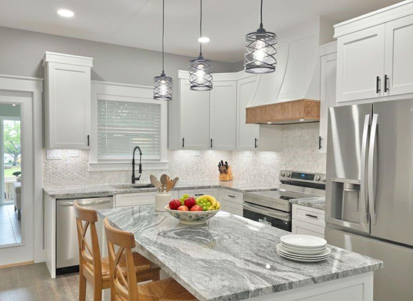 Kitchen with appliances with stainless steel finishes, backsplash, pendant lighting, a center island, and light stone countertops Kitchen with appliances with stainless steel finishes, backsplash, pendant lighting, a center island, and light stone countertops