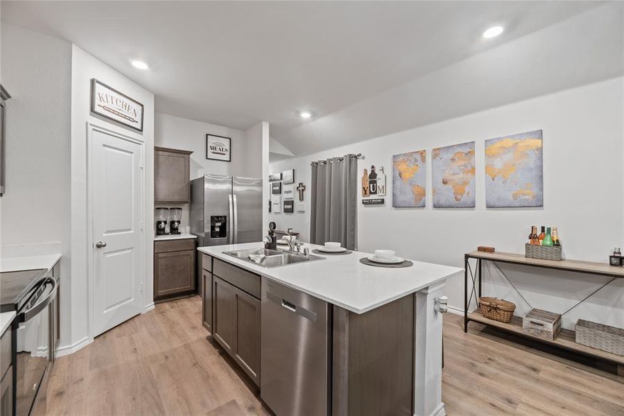 Kitchen with appliances with stainless steel finishes, an island with sink, light wood-style flooring, dark brown cabinets, and recessed lighting