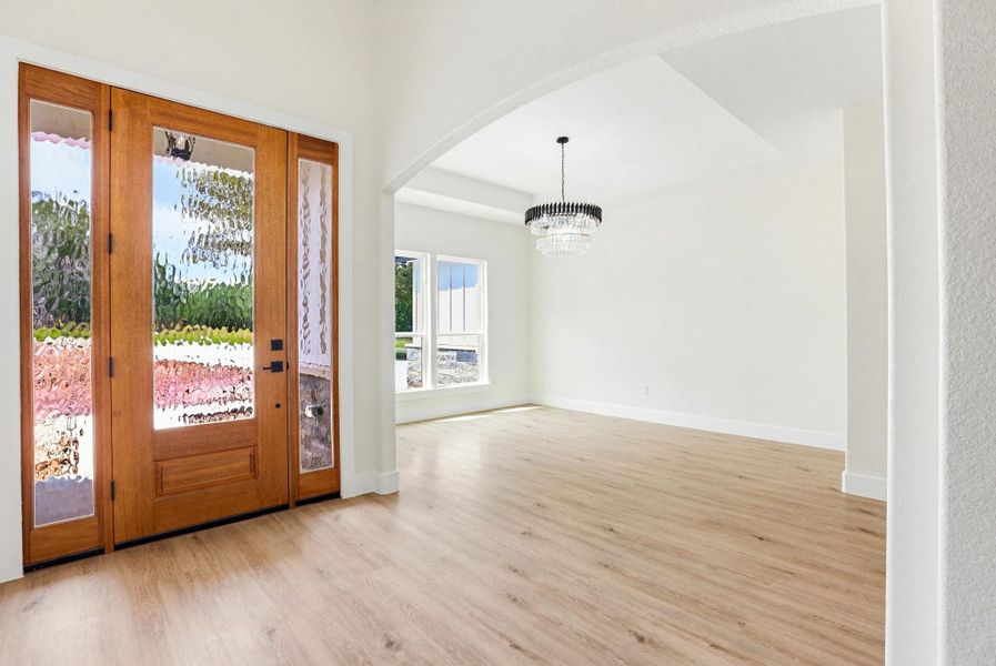 Natural light streams through the stunning entry door, illuminating the seamless flooring of this spacious open-concept room.