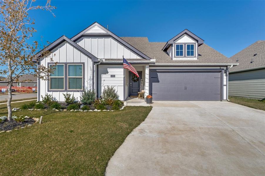 View of front of property with a front yard, concrete driveway, board and batten siding, and a shingled roof
