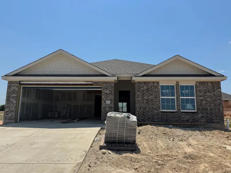 View of front of house featuring an attached garage, concrete driveway, brick siding, and roof with shingles