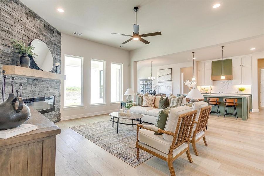 Living room with sink, a fireplace, light wood-type flooring, and ceiling fan with notable chandelier