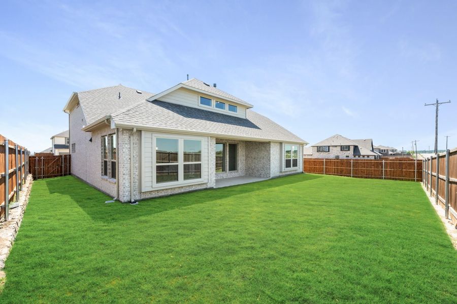 Rear view of brick home with large fenced backyard, green lawn, and covered patio with large windows Rear view of brick home with large fenced backyard, green lawn, and covered patio with large windows