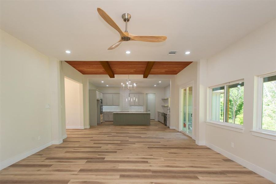 Unfurnished living room featuring ceiling fan with notable chandelier, beamed ceiling, light wood-type flooring, and wooden ceiling