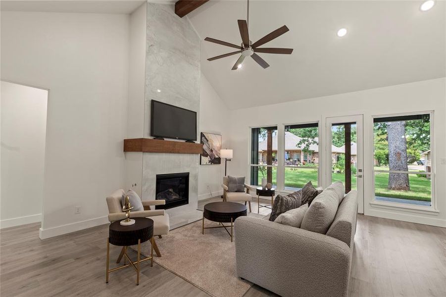 Living area with high vaulted ceiling, a fireplace, wood finished floors, a ceiling fan, and baseboards