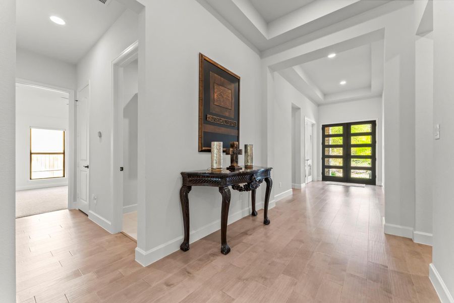 This image shows a hallway with light wood flooring. The front door, with its multiple frosted glass panels, is visible at the end of the hall. This image shows a hallway with light wood flooring. The front door, with its multiple frosted glass panels, is visible at the end of the hall.