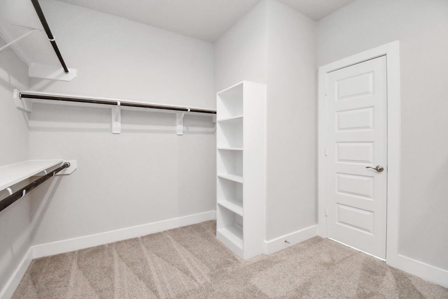 Step into a walk-in closet that defines luxury and functionality. This generously sized space boasts built-in shelving, providing ample room for organization. Sample photo of completed home with similar floor plan. Actual colors and selections may vary.