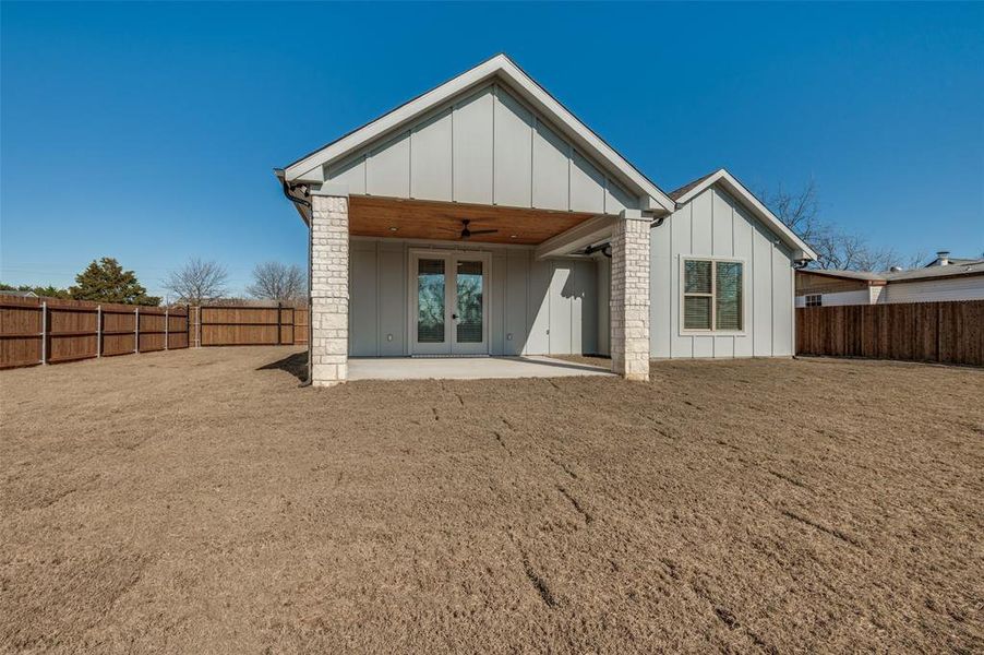 Rear view of property featuring a ceiling fan, board and batten siding, a patio area, a fenced backyard, and french doors