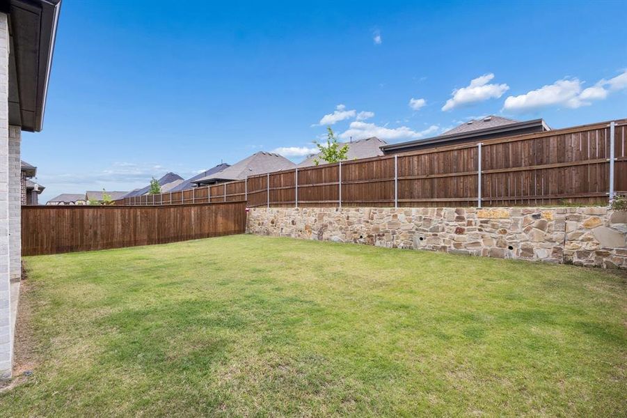 Expansive backyard featuring a manicured lawn, a full-height wood fence, and a decorative stone retaining wall