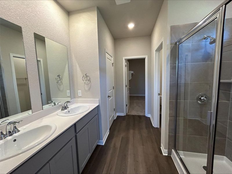 Bathroom featuring wood finished floors, a shower stall, double vanity, and a textured wall Bathroom featuring wood finished floors, a shower stall, double vanity, and a textured wall