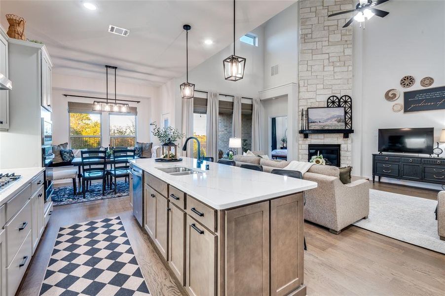 Kitchen with pendant lighting, a stone fireplace, open floor plan, a kitchen island with sink, and high vaulted ceiling
