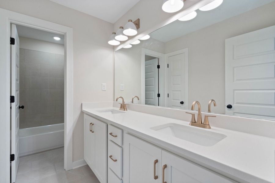 Dual vanity with white shaker cabinetry, gold-tone hardware and fixtures, and a white countertop Dual vanity with white shaker cabinetry, gold-tone hardware and fixtures, and a white countertop