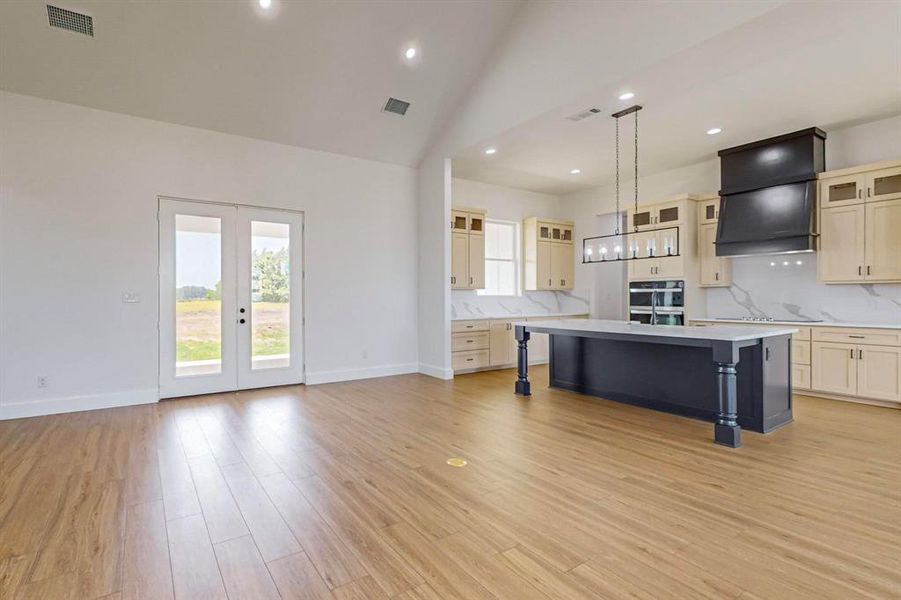 Kitchen featuring light wood-type flooring, a center island, custom exhaust hood, decorative backsplash, and pendant lighting