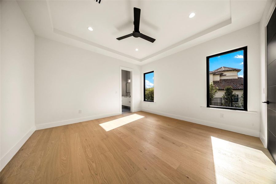 Empty room with a raised ceiling, light wood-style floors, a ceiling fan, and recessed lighting Empty room with a raised ceiling, light wood-style floors, a ceiling fan, and recessed lighting