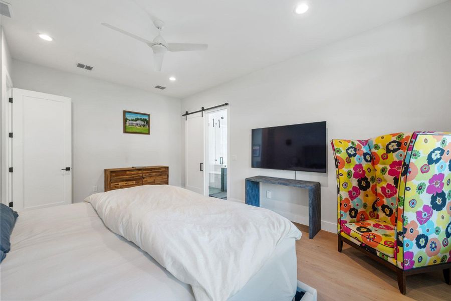 Bedroom with wood finished floors, recessed lighting, a barn door, ceiling fan, and ensuite bath