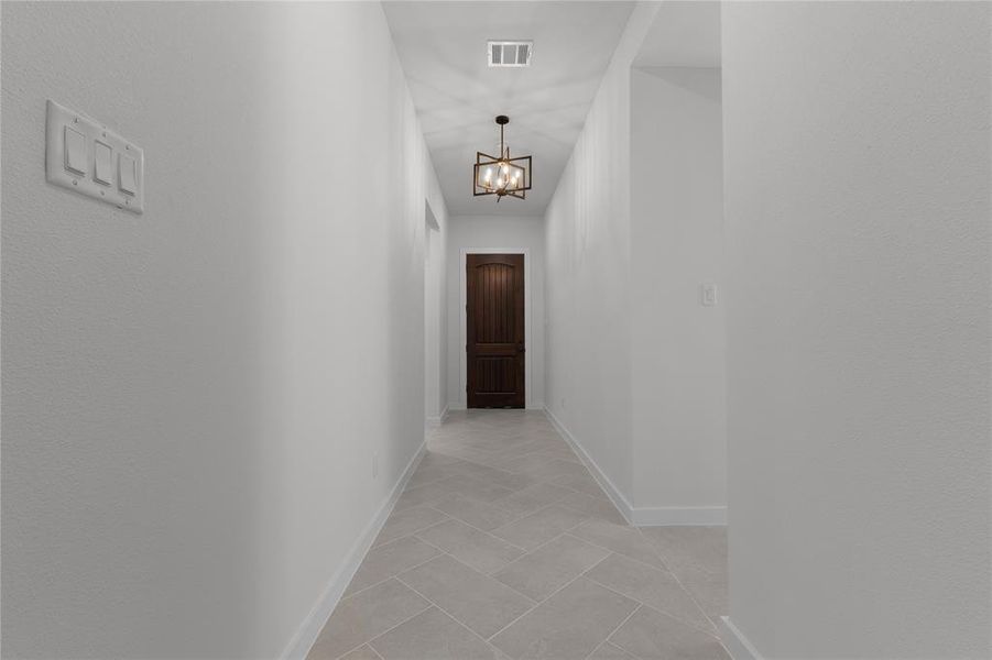 Hallway with light tile patterned flooring and a notable chandelier