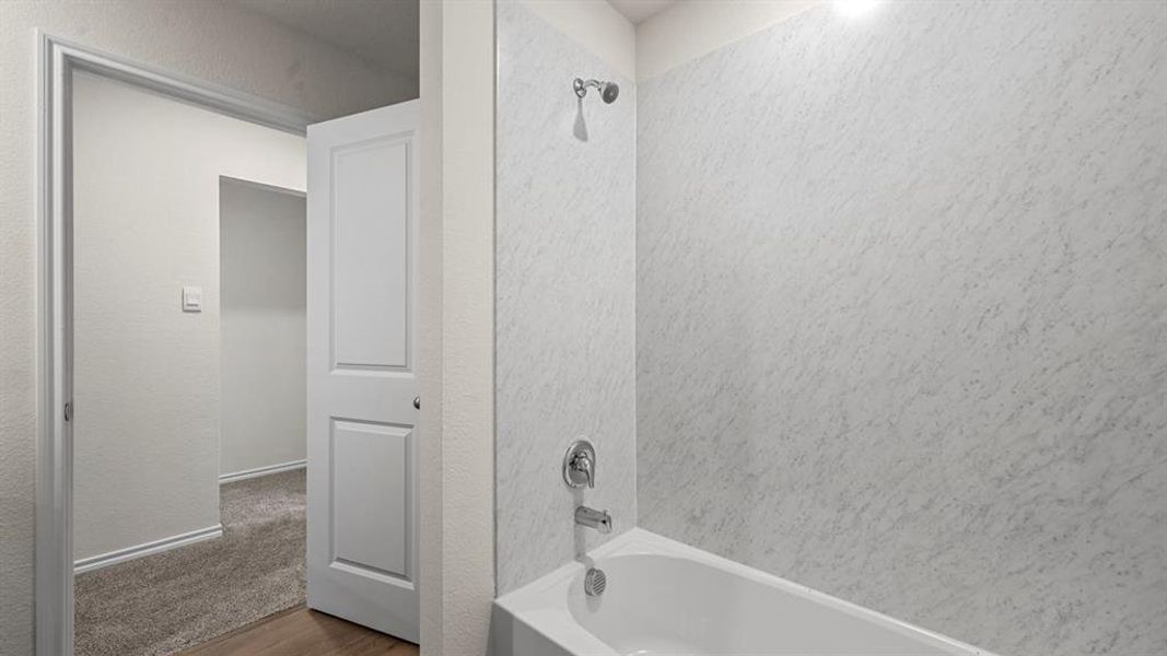 Bathtub and shower combination featuring white textured wall panels and chrome fixtures
