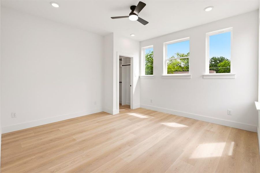 Bright room featuring light wood flooring, white walls, recessed lighting, and a dark-toned ceiling fan
