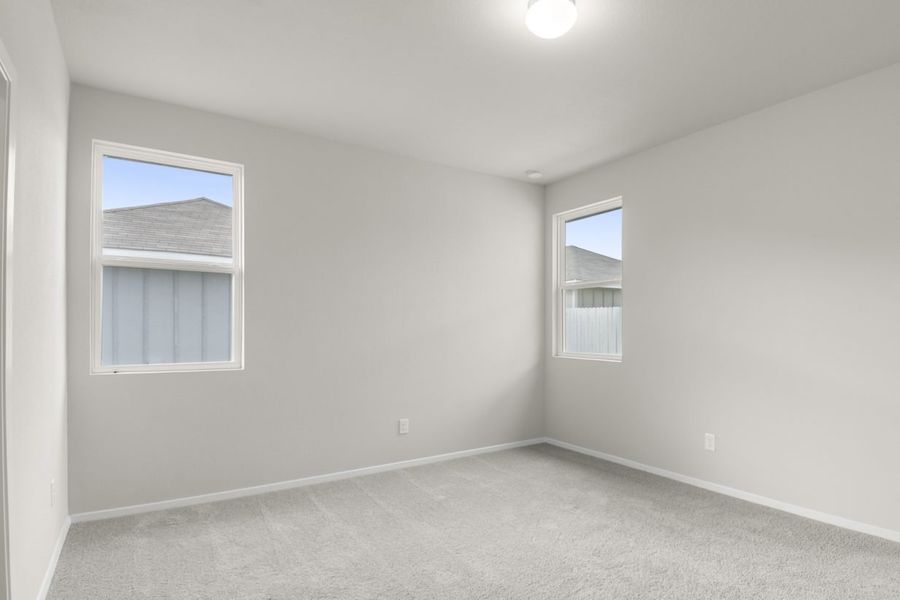 Image of primary bedroom in a one story house with grey carpet and walls with two windows