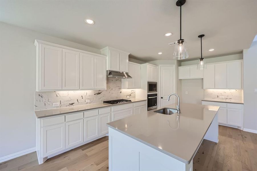 Kitchen featuring stainless steel appliances, sink, light wood-type flooring, and a center island with sink