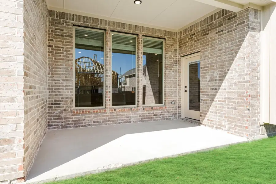 Covered back patio with brick exterior, large windows, and back door entry on concrete slab