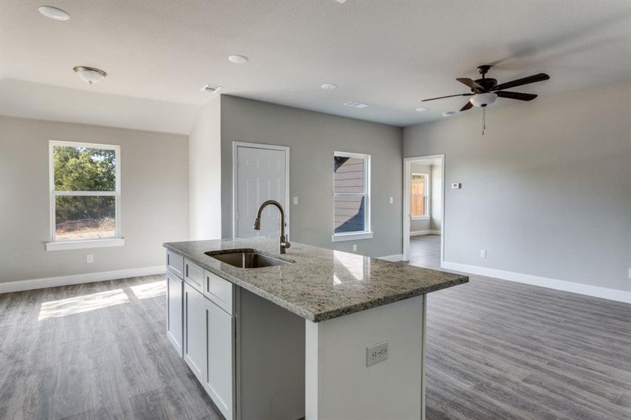 Kitchen with light stone countertops, open floor plan, light wood-style floors, recessed lighting, and a kitchen island with sink