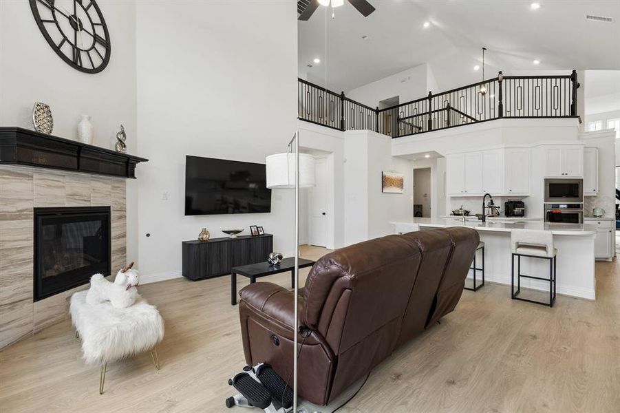 Open-concept living space featuring a fireplace with a mantel, light wood-finish flooring, and a second-story balcony with decorative railings