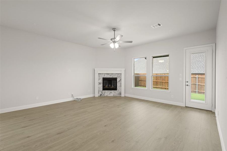 Unfurnished living room featuring healthy amount of natural light, a ceiling fan, a premium fireplace, and wood finished floors