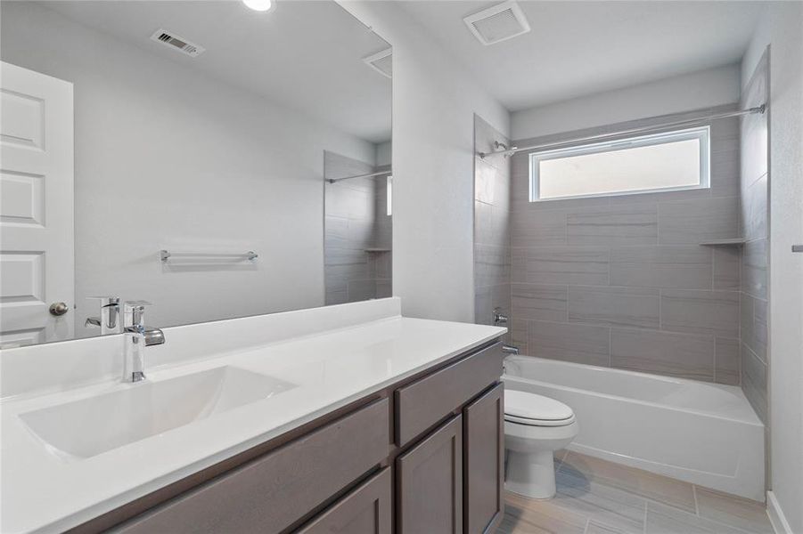 Secondary bath features tile flooring, tub/shower combo with tile surround, stained wood cabinets, beautiful light countertops, mirror, sleek fixtures and modern finishes.