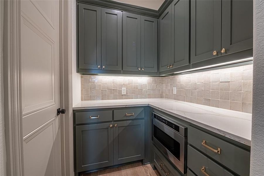 Kitchen with light stone countertops, decorative backsplash, stainless steel microwave, light wood-style floors, and gray cabinets Kitchen with light stone countertops, decorative backsplash, stainless steel microwave, light wood-style floors, and gray cabinets