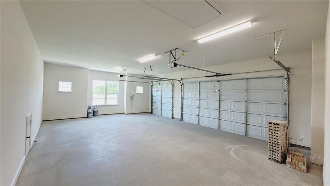 Spacious three-car garage featuring a concrete floor, two white paneled garage doors, and overhead fluorescent lighting