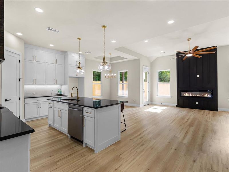 Open-concept living space featuring wood-finish flooring, a contemporary fireplace with a dark paneled accent wall, and a modern ceiling fan