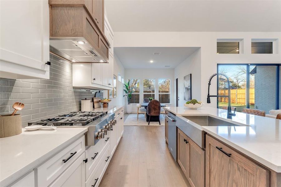 Kitchen featuring light stone counters, white cabinetry, brown cabinetry, stainless steel appliances, and light wood-type flooring Kitchen featuring light stone counters, white cabinetry, brown cabinetry, stainless steel appliances, and light wood-type flooring