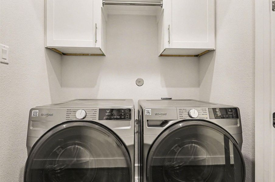 Convenient in-home laundry with upper cabinetry for added storage and organization.