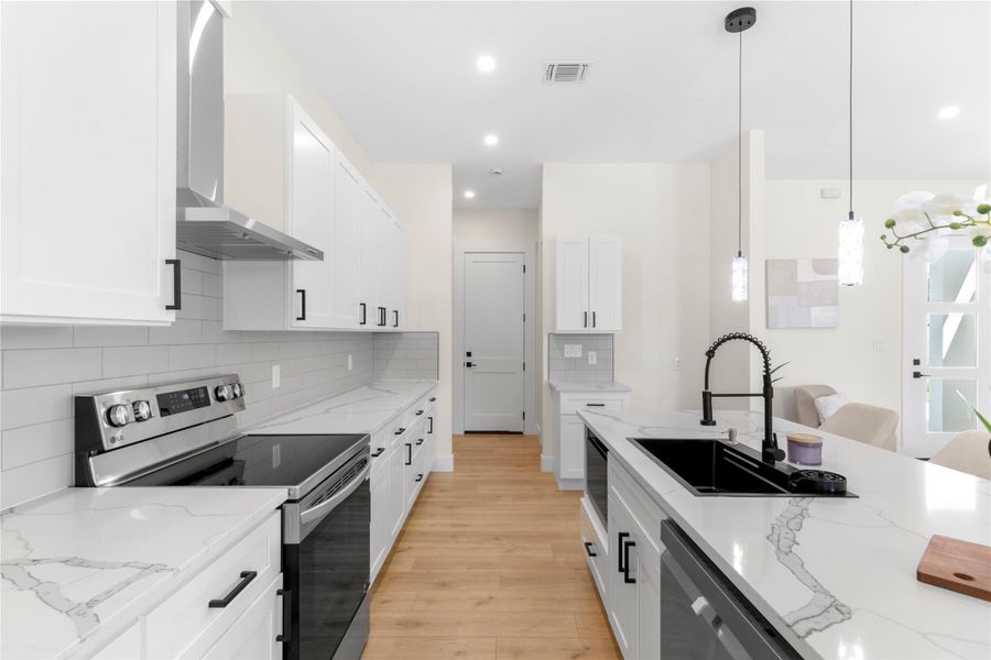 Kitchen with appliances with stainless steel finishes, pendant lighting, light stone countertops, wall chimney exhaust hood, and white cabinets Kitchen with appliances with stainless steel finishes, pendant lighting, light stone countertops, wall chimney exhaust hood, and white cabinets