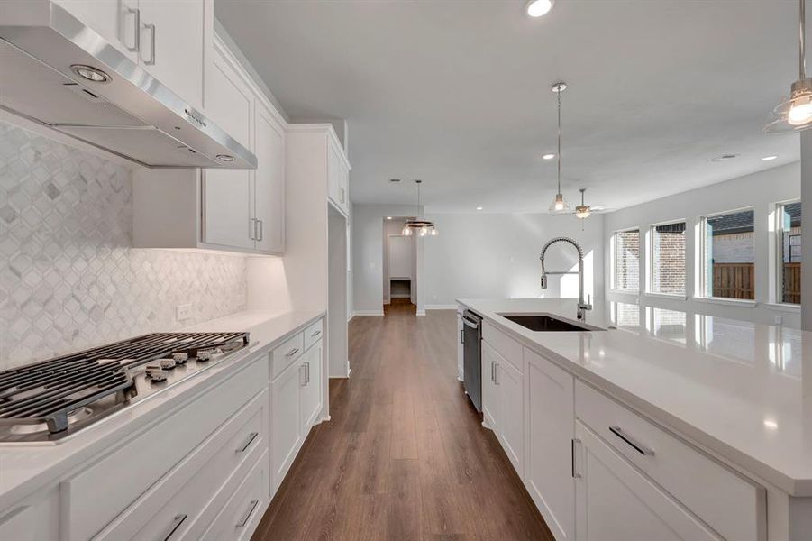 Kitchen featuring white cabinets, stainless steel appliances, an island with sink, hanging light fixtures, and dark wood-style flooring