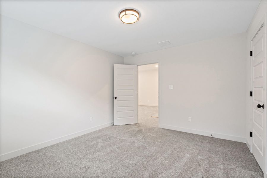 Spacious room featuring neutral carpeting, light-toned walls, white baseboards, a five-panel interior door with matte black hardware, and a ceiling-mounted light fixture Spacious room featuring neutral carpeting, light-toned walls, white baseboards, a five-panel interior door with matte black hardware, and a ceiling-mounted light fixture