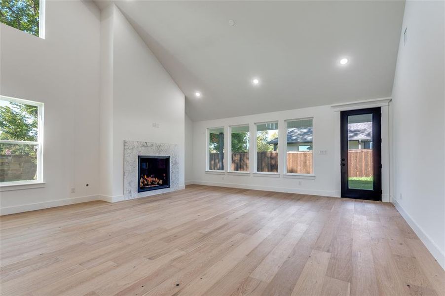 Large Open concept dining and living room with high vaulted ceiling, healthy amount of natural light, recessed lighting, light wood-style flooring, and a premium fireplace