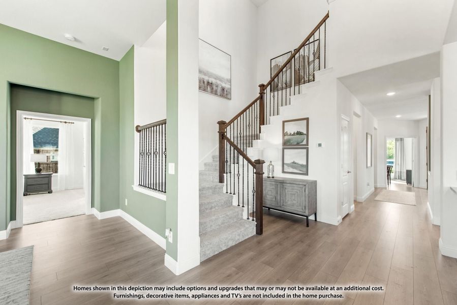 Two-story foyer with carpeted staircase, wood railings, green accent walls, and hardwood floors Two-story foyer with carpeted staircase, wood railings, green accent walls, and hardwood floors