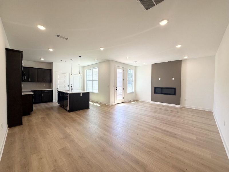Kitchen featuring dark cabinetry, open floor plan, an island with sink, light wood-style floors, and pendant lighting