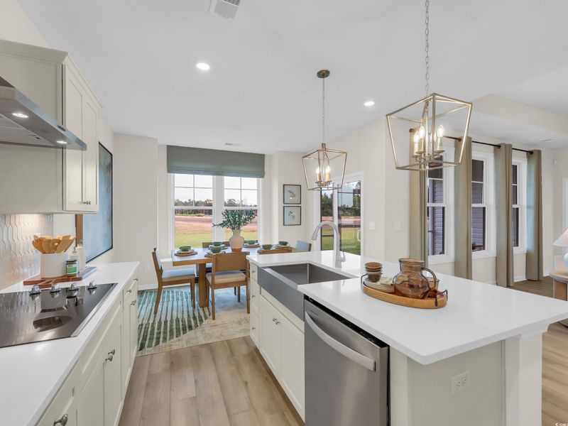 Kitchen featuring light wood-style floors, white cabinets, stainless steel dishwasher, black electric stovetop, and pendant lighting